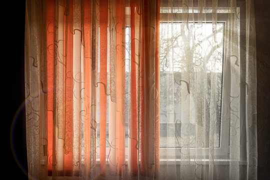 Bright curtain is drawn over a window with a trees behind it in the style of dark and light orange retro filters and translucent color with mixed patterns and split toning.