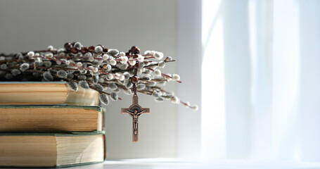 christian rosary cross, biblical books and willow branches on table, abstract light background....