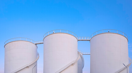 Group of white storage fuel tanks in oil industrial area against blue sky background, low angle view with copy space