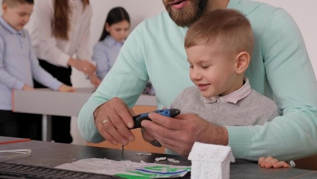 A father and his young son make a 3d plastic model using a 3D pen at school. The concept of teaching children in a computer school. Parents' day at school.