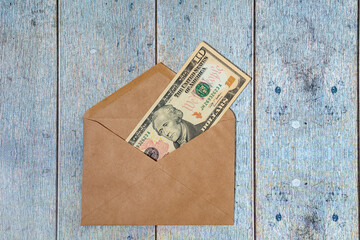 A paper envelope with 10 dollars in it on a light blue wooden background. Flatley