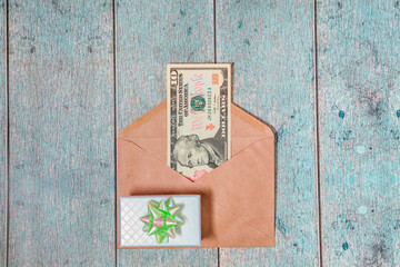 A paper envelope with 10 dollars in it on a light blue wooden background. Flatley with a gift with green ribbon