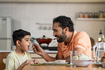 Happy father feeding His child by talking and encouraging at home - concept of fatherhood,...