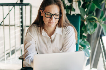 Young attractive redhead wearing glasses business woman working on a laptop. Remote business.