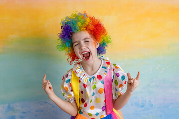 Funny kid clown in a wig playing against a bright wall. 1 April Fool's day concept, birthday concept