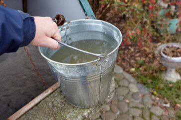 Man hand holding metal bucket with fresh water. Water from a deep well in rural area