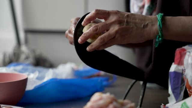 Old Aged hands of chef uses a traditional vegetable cutter to peel potatoes, prepare food for cooking, and emphasize a vegetarian diet concept. low angle, close up