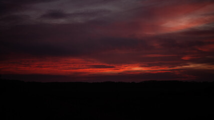 A haunting photo of a dark red sunset adorned with ominous clouds, evoking a sense of foreboding and mystery in the evening sky