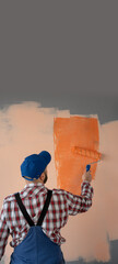Rear view of painter man painting the wall in orange color with paint roller. Banner.