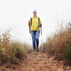 Hiking, woman and walking with trekking pole in a bush path or forest trail for exercise, workout...