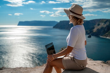 Freelance women sea working on the computer. Good looking middle aged woman typing on a laptop keyboard outdoors with a beautiful sea view. The concept of remote work.