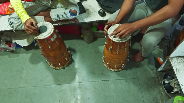 Two people sitting and playing traditional Indian tabla drums with focus on hands and instruments man repairing drum at musical workshop