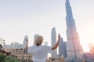 Back view traveler woman arms spread wide on background Dubai skyline with sunlight. Concept UAE...
