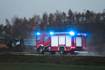 An emergency vehicle drives fast on a road. a firetruck carrying firefighters and fire equipment...