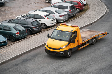 An orange tow truck with a flatbed and a winch at the front is ready to assist a broken car on a...