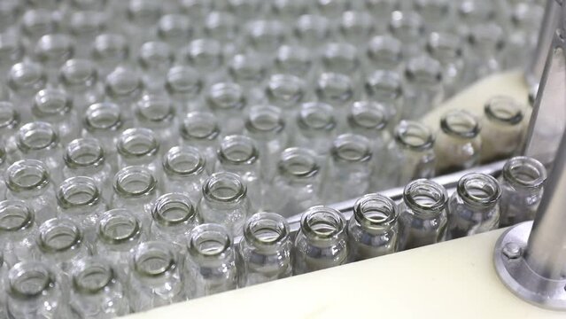 creative close up of empty glass vial bottles moving on a conveyor belt in two rows. medical Injection making process ampoules in a pharmaceutical manufacturing production medicine factory