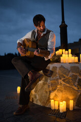 A professional guitarist in a vest plays Spanish guitar. The man is leaning against a street lamp...