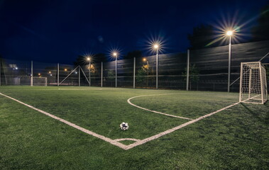 An amateur soccer field with ball illuminated at night. A small football field lit by lanterns in...