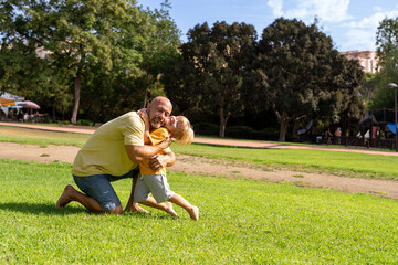 Cheerful father and son looking at each other while laughing at park on sunny day. father and son hugging in the park. communication between father and little son