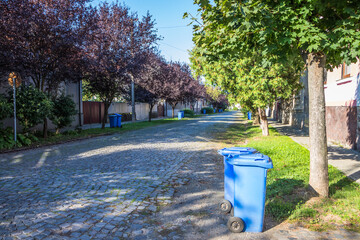 Blue garbage cans on the street in a small town near every house. Centralized garbage collection in a small cozy European city. Garbage collection on a certain day of the week.