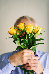 Ein Mann im blauen Hemd hält einen gelben Rosenstrauss vor sein Gesicht. Geschenk, natürliche Person. 