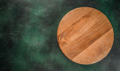 Empty wooden round board, pizza platter on dark green background top view