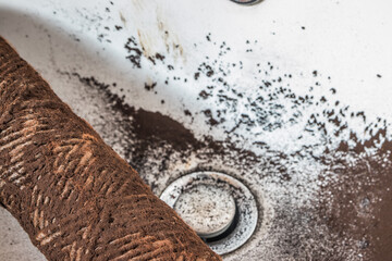 Falling dirty particles from a water filter in a white washbasin. Elements of a filtration system...