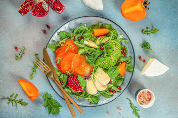 Healthy salad with persimmon, fresh greens, avocado, Camembert cheese and pomegranate. top view. copy space for text