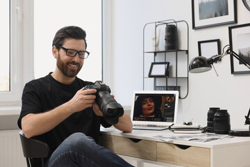 Professional photographer in glasses holding digital camera at table in office