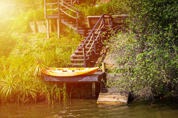 Bright yellow kayak drying on a private jetty hidden in the lush green at the bottom of a steep...