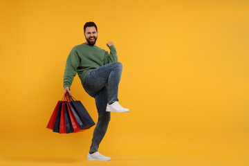 Excited man with many paper shopping bags on orange background. Space for text