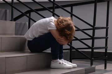 Child abuse. Upset boy sitting on stairs