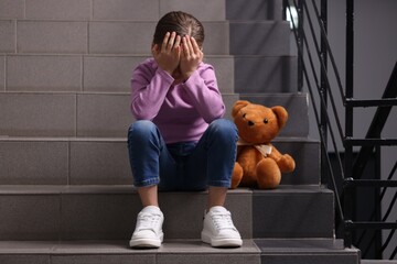 Child abuse. Upset girl with toy sitting on stairs