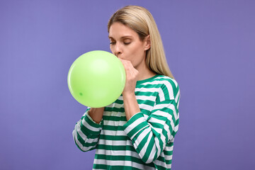 Fototapeta premium Woman blowing up balloon on violet background
