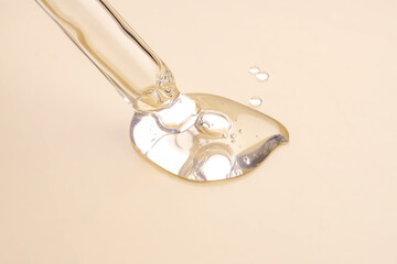 A cosmetic product gel or collagen serum flows out of a pipette with bubbles on beige background.