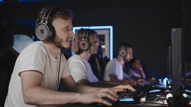 Gamers playing video game on PC at computer club cyber sport tournament. E-sport championship. Players in headset. Bristly captain gives instructions to team over mic. Multiplayer online tactics
