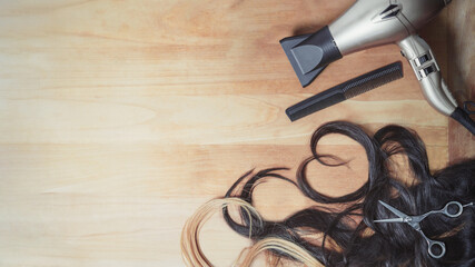 Hairdresser tools and piece of wavy dark hair and blonde hair with copy space on the wooden background. Heart shape. - obrazy, fototapety, plakaty