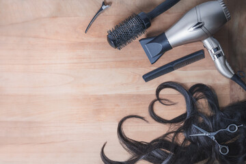 Hairdresser tools and piece of wavy dark hair with copy space on the wooden background. Heart shape.