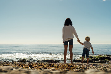 young mother and son stand on the seashore. A woman with a child stands on the beach, rest and...