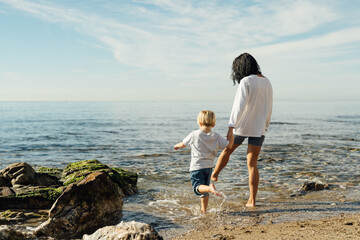 mother and son go into the sea. mother and son test the water with bare feet. mother and son having...