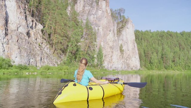 Woman traveler swims in boat on mountain river surrounded by high mountains. Girl kayak rafting rowing leisurely paddle along calm river. Packrafting