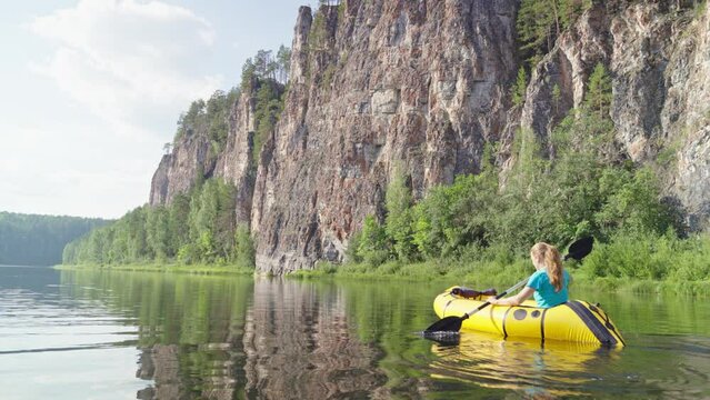 Woman traveler swims in boat on mountain river surrounded by high mountains. Girl kayak rafting rowing leisurely paddle along calm river. Packrafting
