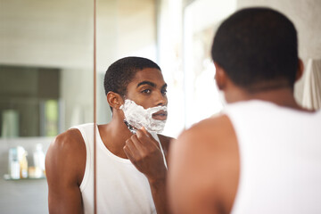 Black man, mirror and shaving with razor in bathroom for grooming, skincare or morning routine. Reflection, beard or person with cream on face for cleaning, health or hair removal for hygiene in home - obrazy, fototapety, plakaty