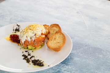 Salmon tartare with boiled egg, avocado, tomato jam and black olive tapenade. Over a sky blue grunge background.