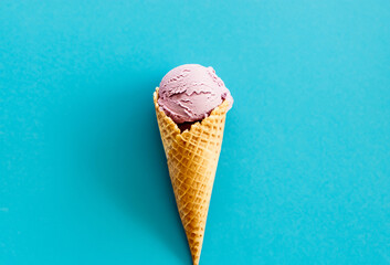 Strawberry ice cream in waffle cone on blue background.