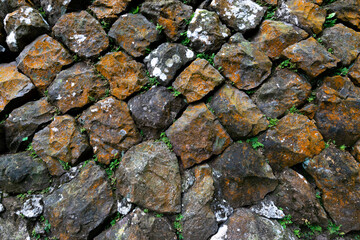 Old stone wall with many rust spot on it, and some green plants living in between, in Jinguashi, New Taipei City, Taiwan.