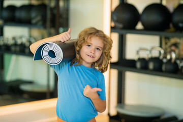 Fototapeta na wymiar Fit kid holding yoga mat in gym. Yoga kids concept. Strong sporty athletic fitness child. Kids Workout sport concept.