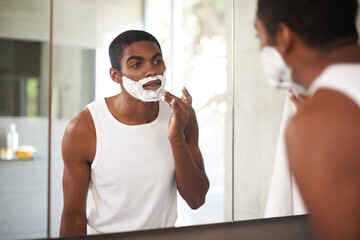 Black man, mirror and shaving cream on face in bathroom for grooming, skincare or morning routine....