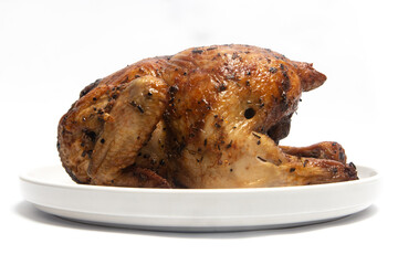A whole delicious roasted chicken seasoned with herbs in a white plate isolated on white background clipping path