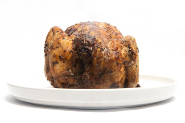 A whole delicious roasted chicken seasoned with herbs in a white plate isolated on white background clipping path
